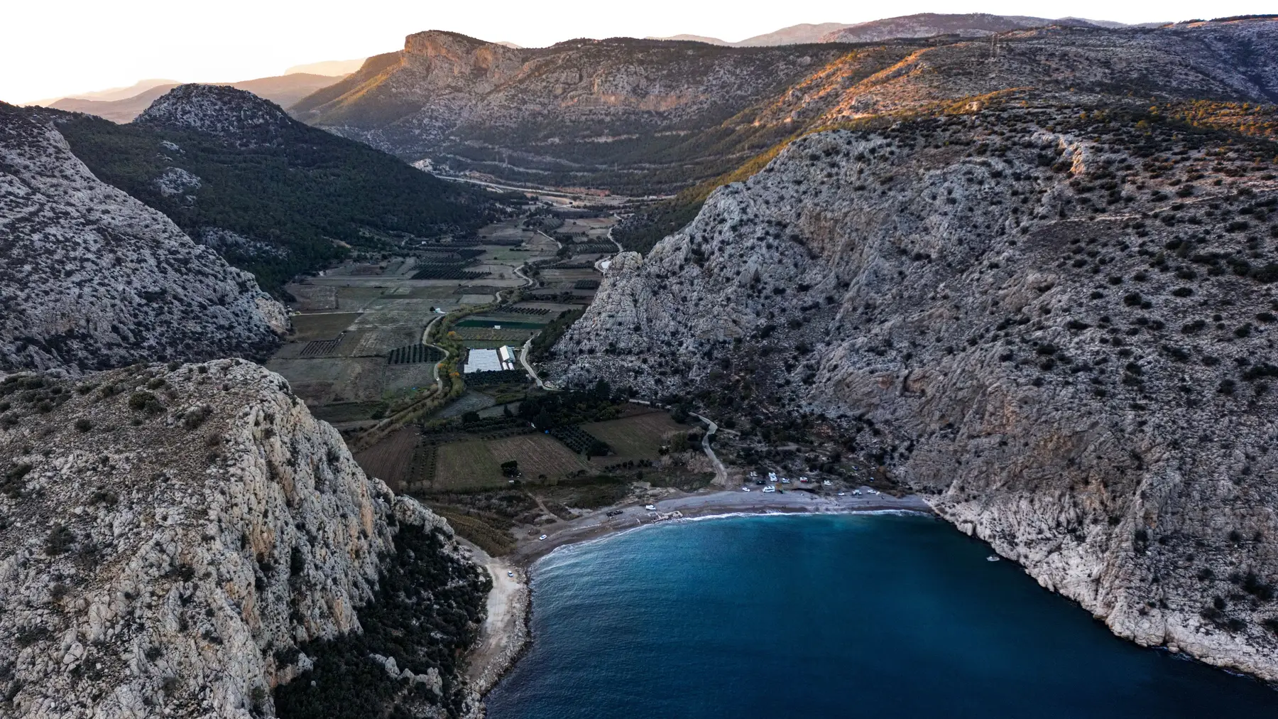 Aerial view of a coastal mountain valley, its layered cliffs terracing down to meet the sea.